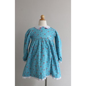 May include: A light blue dress with a white collar and pink floral print. The dress has long sleeves and a gathered skirt. The dress is made of a soft, comfortable fabric and has a lace trim.
