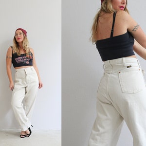Pu&ograve; includere: Una donna indossa una canotta nera con una stampa grafica e un berretto rosso, abbinato a jeans dritti beige chiaro a vita alta.