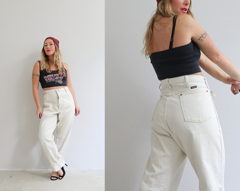 Pu&ograve; includere: Una donna indossa una canotta nera con una stampa grafica e un berretto rosso, abbinato a jeans dritti beige chiaro a vita alta.