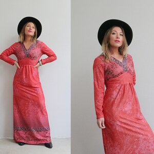 May include: A woman wearing a long, red maxi dress with a floral print and a black wide-brimmed hat. The dress has a V-neckline and long sleeves.