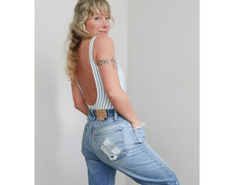 May include: A light blue and white striped bodysuit with a low back is paired with light wash denim jeans. The jeans have distressed details and a classic five-pocket design. The model is wearing a vintage Levi's jeans.