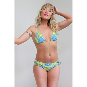 May include: A bikini set in a yellow, blue, and white plaid pattern. The top is a triangle style with thin straps, and the bottoms have tie sides. The swimwear features a classic plaid design, suitable for swimming or sunbathing.