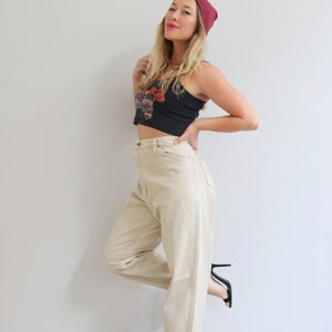 May include: A woman wearing a black crop top with a floral design, high-waisted beige pants, and black heeled sandals. She is also wearing a burgundy beanie.