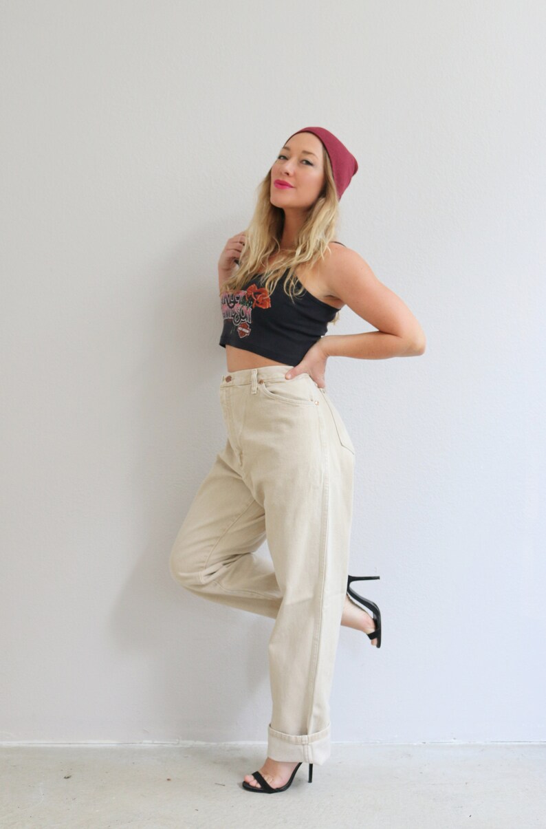 May include: A woman wearing a black crop top with a floral design, high-waisted beige pants, and black heeled sandals. She is also wearing a burgundy beanie.
