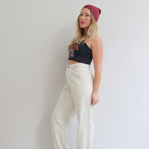 Pu&ograve; includere: Una donna indossa un paio di jeans bianchi a vita alta con orli arrotolati, un top corto nero con un motivo floreale e un berretto bordeaux.