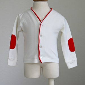 May include: White cardigan with red trim and red elbow patches. The cardigan has a button closure.