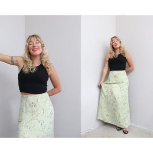 May include: A black sleeveless crop top paired with a floor-length light green skirt featuring a delicate dark green floral pattern. The skirt has a high waist and a straight silhouette that extends to the floor, creating a simple two-piece outfit.