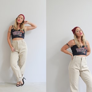 May include: A woman wearing a black crop top with a graphic print, a burgundy beanie, and high-waisted beige pants. She is standing with her hands on her hips.