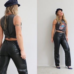 May include: A woman wearing a black leather pants, a gray tank top with a graphic print, and a navy blue cap.