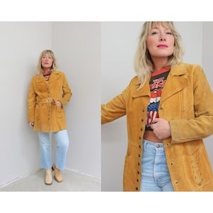 May include: Mustard yellow suede jacket with a button-up front, notched lapels, and a matching belt. The jacket has pockets and decorative stitching. A vintage-inspired piece.