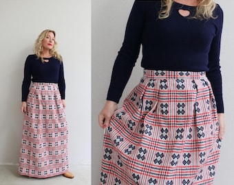 Puede incluir: Una falda larga y plisada con estampado de cuadros rojo, blanco y azul. La falda está hecha de una tela gruesa y tejida y tiene una cintura alta.