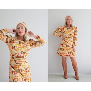 May include: A vintage 70s style dress with a peach background and a pattern of brown, orange, and yellow strawberries. The dress has long sleeves with puffed shoulders and a mini length.