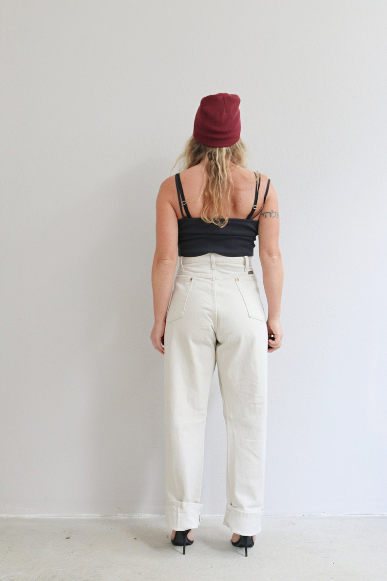 Pu&ograve; includere: Una persona indossa un paio di jeans bianchi a vita alta con orli arrotolati, una canotta nera e un berretto bordeaux.