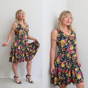 May include: A sleeveless black dress with a V-neck, adorned with a vibrant floral pattern in yellow, pink, and blue. The dress has a flared skirt and a knee-length hemline, perfect for a summer day.