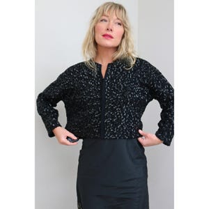 May include: A black sequined jacket with long sleeves and a zipper closure. The jacket is paired with a black skirt. The woman in the image is wearing the jacket.