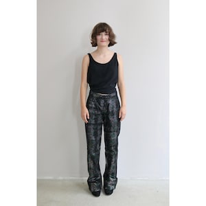 Puede incluir: Una mujer con un top negro de tirantes y pantalones negros con un patrón iridiscente brillante. Los pantalones tienen un estilo de pierna ancha.