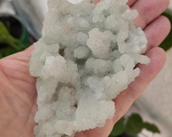 May include: A cluster of light green and white crystal formations, resembling a small, rocky mountain. The crystals are translucent and have a rough, textured surface.