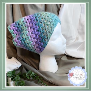 May include: A multi-coloured crochet headband in shades of purple, teal, and green. The open weave design is displayed on a white mannequin head. A fashionable accessory for any season.