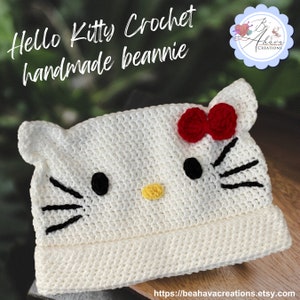 May include: A handmade, cream-coloured crochet beanie with a Hello Kitty design. The beanie has black eyes, a yellow nose, and a red bow. The text "Hello Kitty Crochet handmade beanie" is displayed at the top of the image.