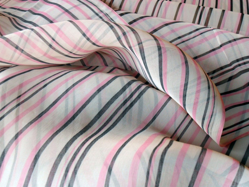 Pode incluir: Close-up de um tecido transparente com um padr&atilde;o listrado. O tecido apresenta listras alternadas rosa, pretas e cinzas sobre um fundo branco. O tecido &eacute; drapeado, criando dobras e curvas suaves.