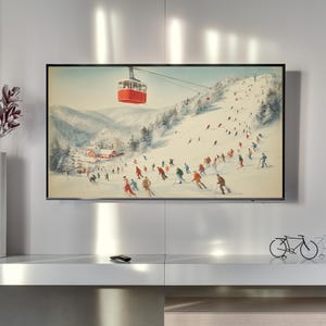 Puede incluir: Una impresión enmarcada que representa una escena de estación de esquí vintage. La obra de arte presenta esquiadores en una ladera nevada, un teleférico rojo y un pequeño pueblo. La paleta de colores incluye blanco, rojo y varias tonalidades de azul y verde.