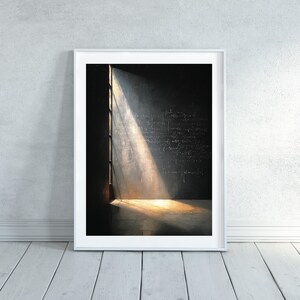 May include: A framed art print depicting a beam of light illuminating a dark room. The light shines through a window, highlighting equations written on the wall. The artwork is in a white frame and rests on a white wooden floor.
