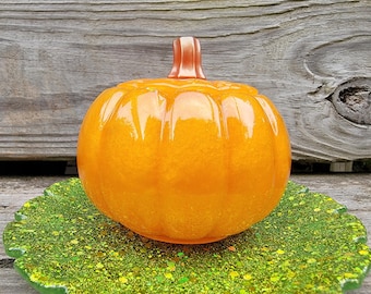 May include: A shiny orange pumpkin-shaped dish with a green glitter-covered base. The dish is made of resin and has a glossy finish.