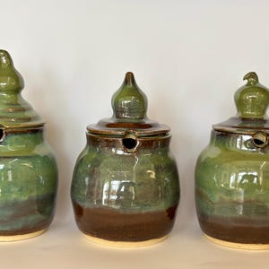 May include: Three ceramic jars with green and brown glaze. Each jar has a unique, bulbous lid.
