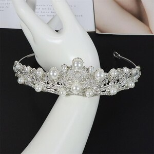 Pu&ograve; includere: Una tiara color argento con perle finte e strass trasparenti. La corona presenta un delicato design traforato con un gruppo centrale di perle pi&ugrave; grandi e perle pi&ugrave; piccole. La tiara &egrave; progettata per essere indossata sulla testa.