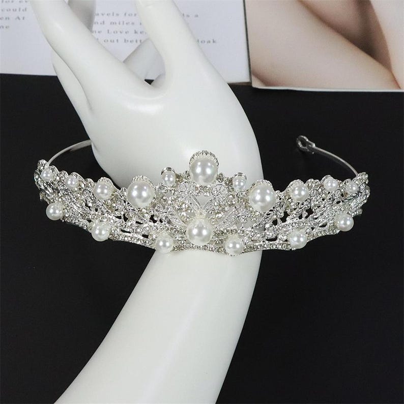 Pu&ograve; includere: Una tiara color argento con perle finte e strass trasparenti. La corona presenta un delicato design traforato con un gruppo centrale di perle pi&ugrave; grandi e perle pi&ugrave; piccole. La tiara &egrave; progettata per essere indossata sulla testa.