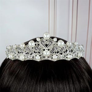 Pu&ograve; includere: Tiara argentata con perle finte e strass trasparenti. La corona presenta un delicato design a filigrana con perle grandi e rotonde e pietre pi&ugrave; piccole. Un copricapo da sposa o per occasioni speciali.