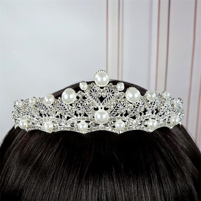 Pu&ograve; includere: Tiara argentata con perle finte e strass trasparenti. La corona presenta un delicato design a filigrana con perle grandi e rotonde e pietre pi&ugrave; piccole. Un copricapo da sposa o per occasioni speciali.