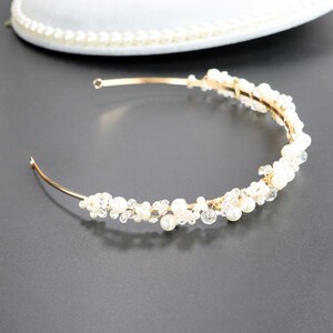 May include: A delicate gold-toned bridal headband. The headband is adorned with clusters of white pearls and clear crystals. The design is elegant and suitable for weddings or special occasions. The headband is curved and has a simple, refined aesthetic.