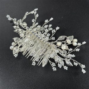 Op de afbeelding: Zilverkleurige bruidshaarkam met delicate bloemen- en bladeraccenten. De kam heeft kleine witte kralen en imitatieparels, wat een elegant en romantisch ontwerp cre&euml;ert. Perfect voor bruiloften of speciale gelegenheden.