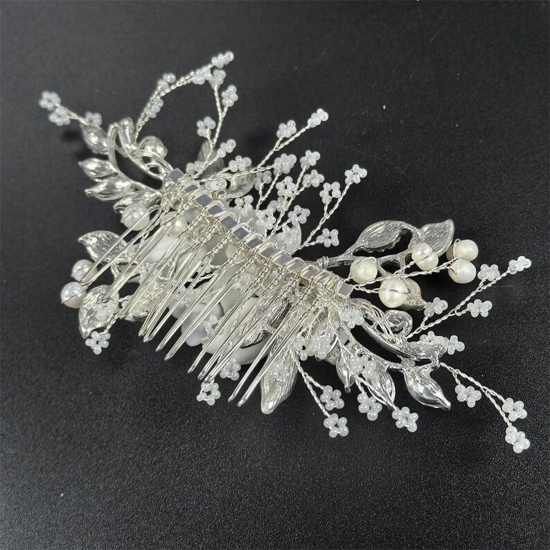 Op de afbeelding: Zilverkleurige bruidshaarkam met delicate bloemen- en bladeraccenten. De kam heeft kleine witte kralen en imitatieparels, wat een elegant en romantisch ontwerp cre&euml;ert. Perfect voor bruiloften of speciale gelegenheden.