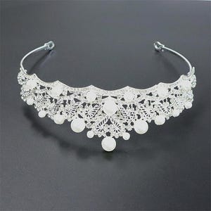 Pu&ograve; includere: Tiara nuziale color argento con un delicato design traforato. La tiara &egrave; adornata da numerosi cristalli trasparenti e grandi perle finte bianche rotonde. La tiara ha una forma curva ed &egrave; progettata per essere indossata sulla testa.