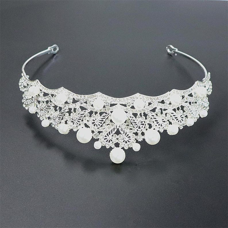 Pu&ograve; includere: Tiara nuziale color argento con un delicato design traforato. La tiara &egrave; adornata da numerosi cristalli trasparenti e grandi perle finte bianche rotonde. La tiara ha una forma curva ed &egrave; progettata per essere indossata sulla testa.