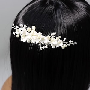 May include: A delicate white floral hair comb featuring small fabric flowers, faux pearls, and crystal accents. The bridal hair accessory is set on a silver-toned wire base, perfect for weddings or special occasions.