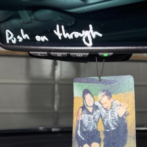 May include: A car air freshener with a photo of two people wearing skeleton costumes. The text "Push on through" is written on the rearview mirror of the car.