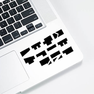 Peut inclure: Un ordinateur portable blanc avec un clavier noir et une série de formes géométriques noires disposées sur le pavé tactile. Les formes semblent épeler un mot ou une phrase, avec une esthétique moderne et minimaliste.