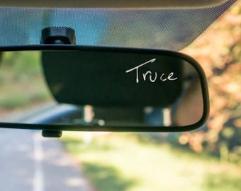 Può includere: Uno specchietto retrovisore con la parola "Truce" scritta sopra con un pennarello bianco.