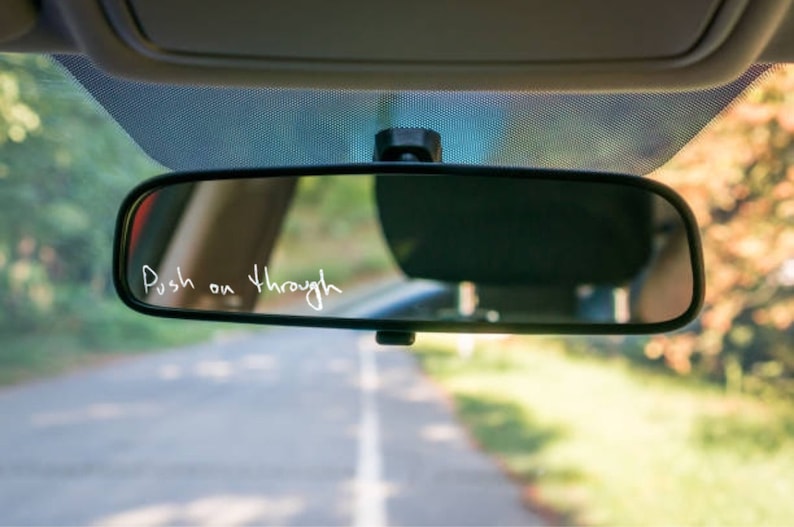 Pu&ograve; includere: Uno specchietto retrovisore in un'auto con le parole "Push on through" scritte sullo specchio con un pennarello bianco.