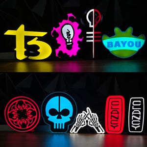 May include: A collection of illuminated signs in various shapes and colors. The signs include a yellow stylized "T3", a pink lightbulb, a green "BAYOU" sign, a red floral design, a blue skull, and a pair of skeleton hands.
