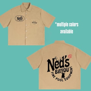 May include: A tan short-sleeve button-down shirt. The front features a black oval logo reading Ned's Bayou and a small creature graphic on the pocket. The back displays a large black logo reading Ned's Bayou Fine Pool Equipment with a rose.