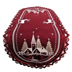 May include: Red oval table runner with white embroidered Christmas village scene, including a church, trees, and reindeer. The runner has a scalloped edge.