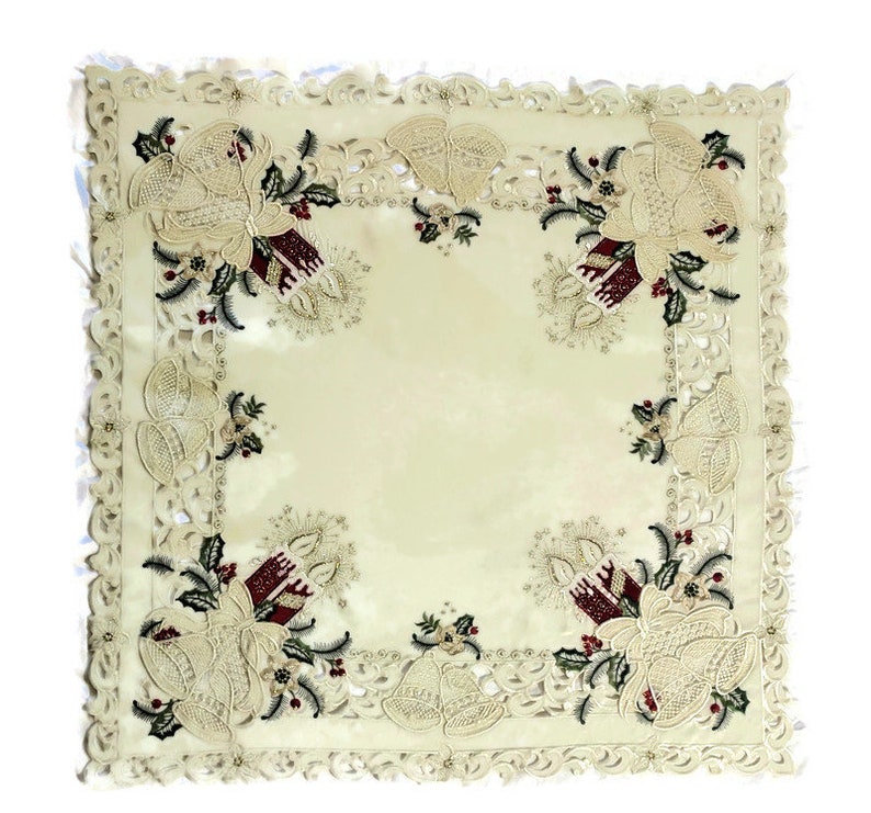 Puede incluir: Un camino de mesa blanco con un delicado dise&ntilde;o de encaje y motivos navide&ntilde;os bordados. El dise&ntilde;o presenta acebo rojo y verde, campanas doradas y velas.