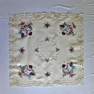 K&ouml;nnte beinhalten: Eine wei&szlig;e Tischdecke mit einer zarten Spitzenbord&uuml;re und gestickten Schneemann-Motiven. Die Tischdecke zeigt ein zentrales Design eines Schneemanns mit einem roten Schal und einem gr&uuml;nen Kranz. Die Tischdecke ist perfekt f&uuml;r ein Weihnachtsessen oder eine Feiertagsfeier.