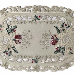 Puede incluir: Caminero de mesa ovalado de color marfil con un delicado borde de encaje. El centro presenta un dise&ntilde;o bordado de campanas de Navidad, velas y ramas de acebo en tonos rojos, verdes y dorados.