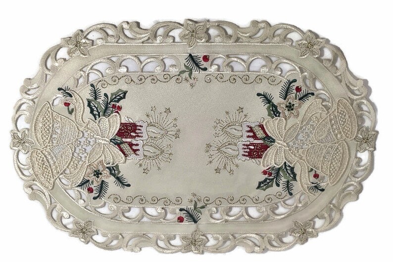 Puede incluir: Caminero de mesa ovalado de color marfil con un delicado borde de encaje. El centro presenta un dise&ntilde;o bordado de campanas de Navidad, velas y ramas de acebo en tonos rojos, verdes y dorados.