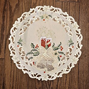 Puede incluir: Camino de mesa de encaje blanco con un delicado dise&ntilde;o floral y un tema navide&ntilde;o. El dise&ntilde;o presenta velas rojas y blancas, campanas y acebo.
